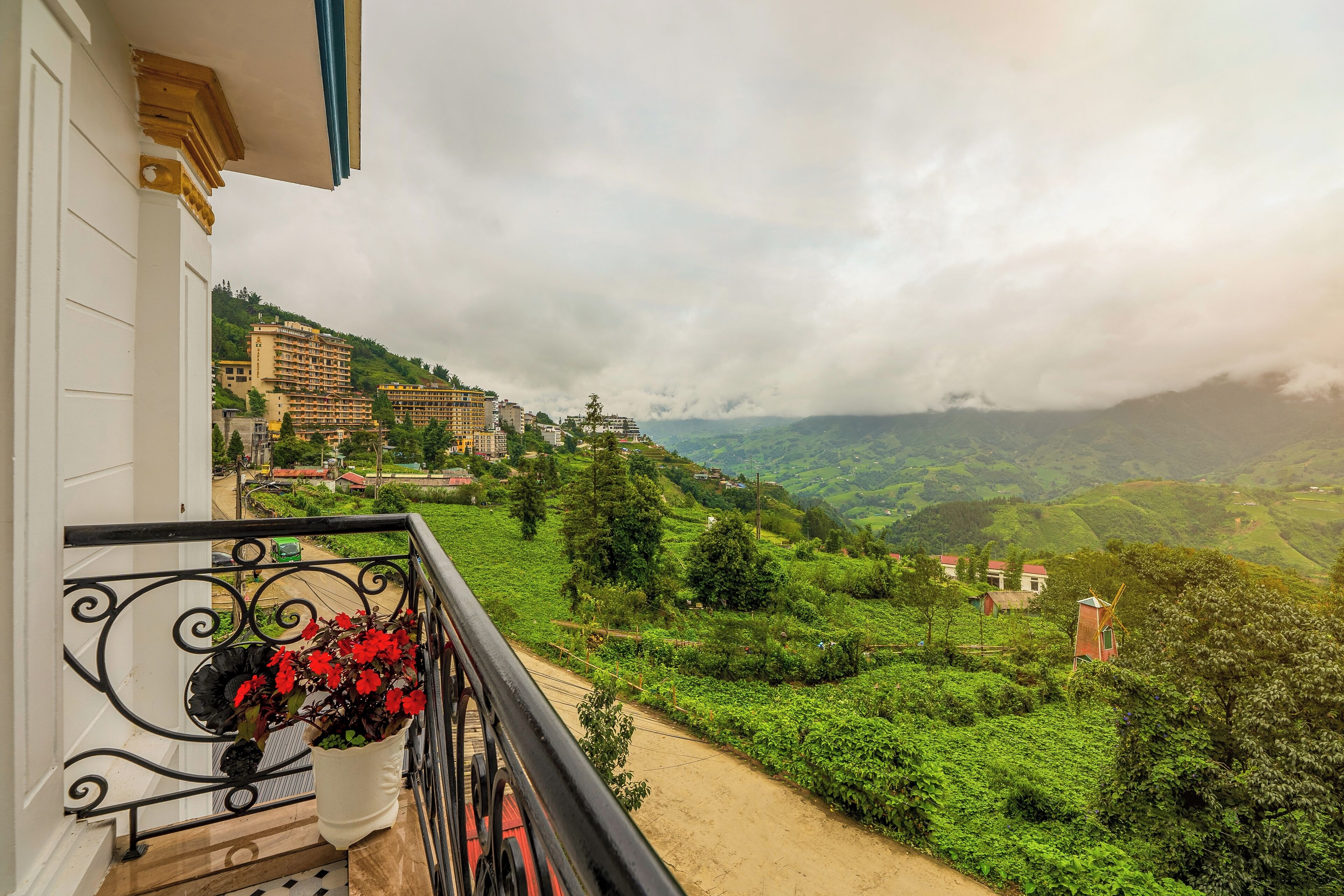 Un balcone con una pianta in vaso, con vista su una rigogliosa valle verde e edifici sullo sfondo.