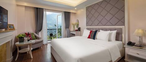 A modern hotel room with a large bed, a desk, a chair, and a balcony with a mountain view.