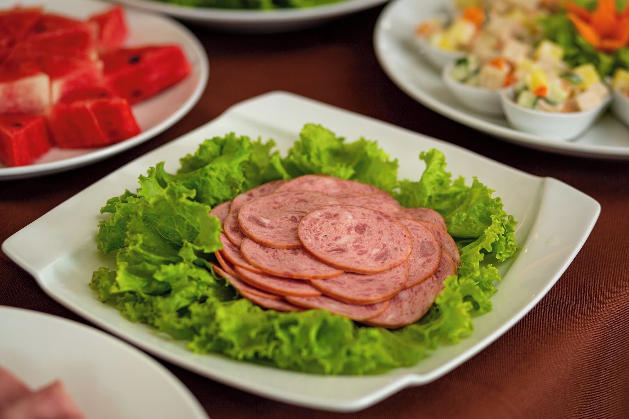 A plate of sliced meat on lettuce with other dishes in the background.