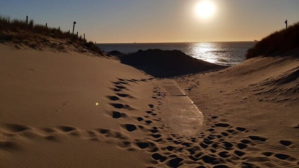 Ein Sandweg am Strand, der zum Meer führt, mit Fußabdrücken und einem Betonweg.