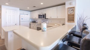 Una cocina moderna con armarios blancos, un microondas de acero inoxidable y una isla grande con taburetes de bar.