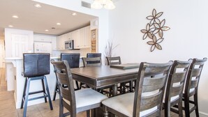 Un comedor con mesa y sillas de madera, una cocina al fondo y un adorno decorativo en la pared.
