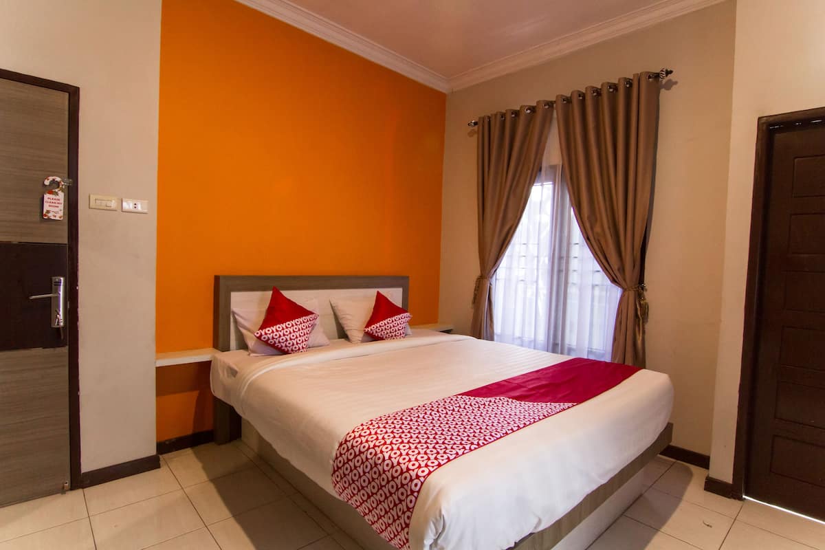 A hotel room with a large bed, orange walls, and a window with curtains.