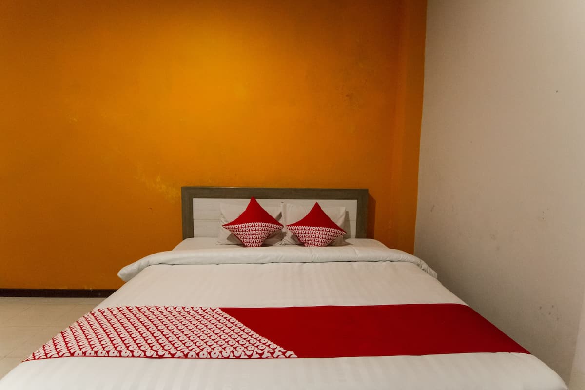 A bed with a white and red bedspread, two red pillows, and a wooden headboard.