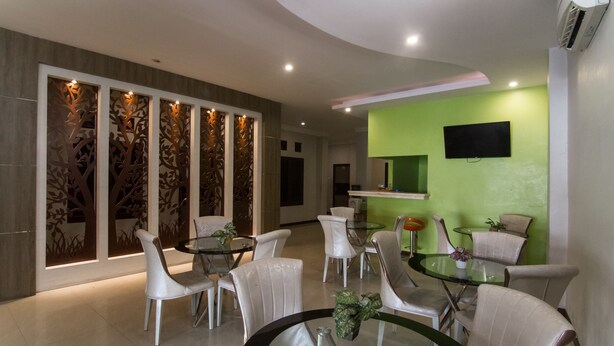 A modern dining area with white chairs and glass tables, a green accent wall, and a mounted TV.