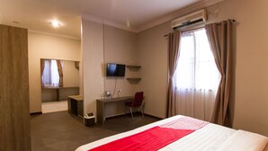 A hotel room with a bed, a desk, a chair, a TV, and an air conditioning unit.
