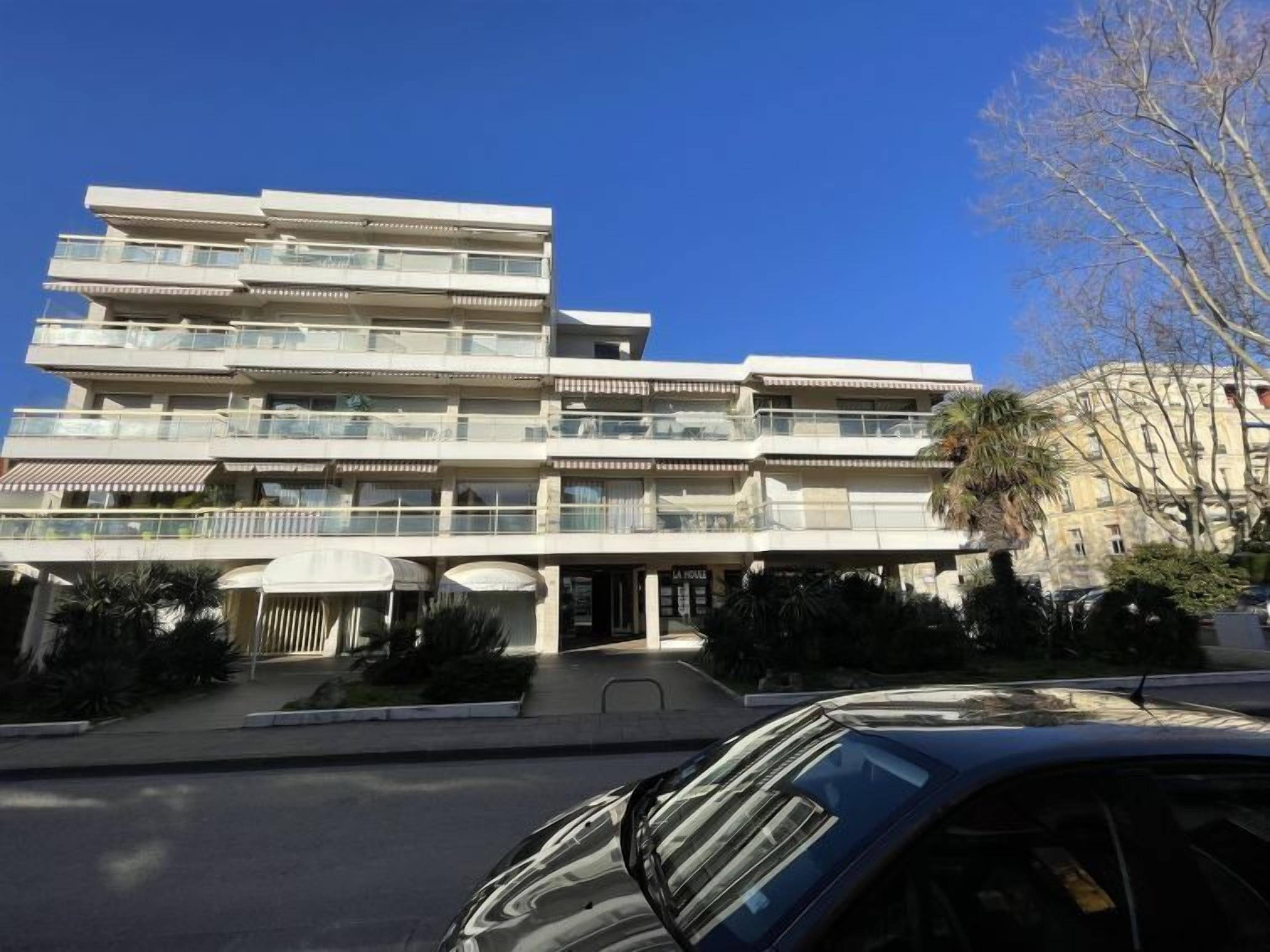 A multi-story hotel with balconies, a covered entrance, and a parking area.