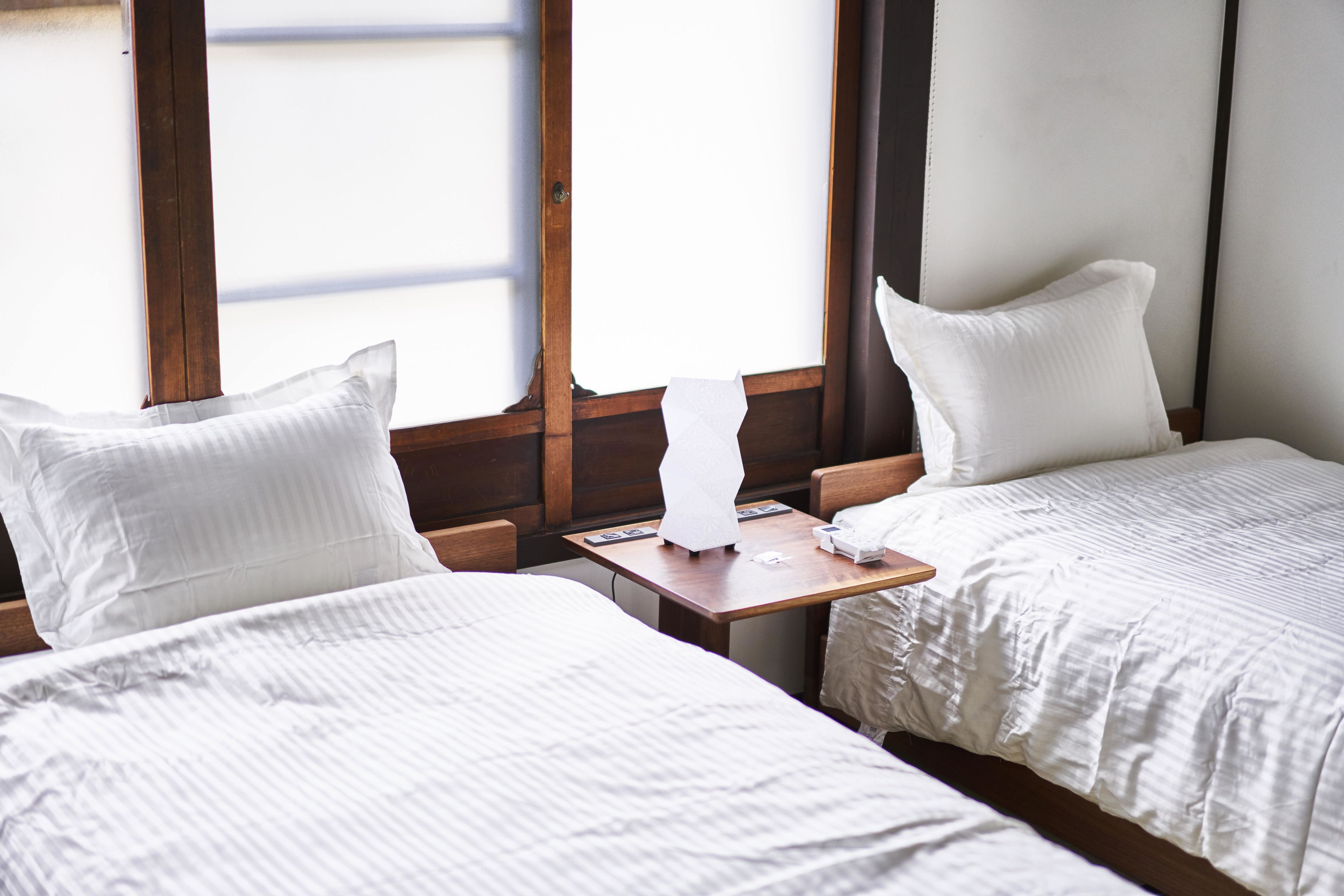 A hotel room with two beds, a wooden nightstand, and a window with blinds.