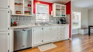 Cocina con armarios blancos, lavavajillas de acero inoxidable y una pared de acento roja.