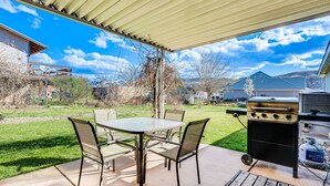 Un patio al aire libre con mesa y sillas, una parrilla y un tanque de propano.
