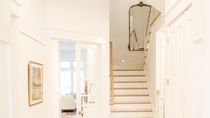 A hallway with wooden flooring, white walls, and a staircase leading to another room.