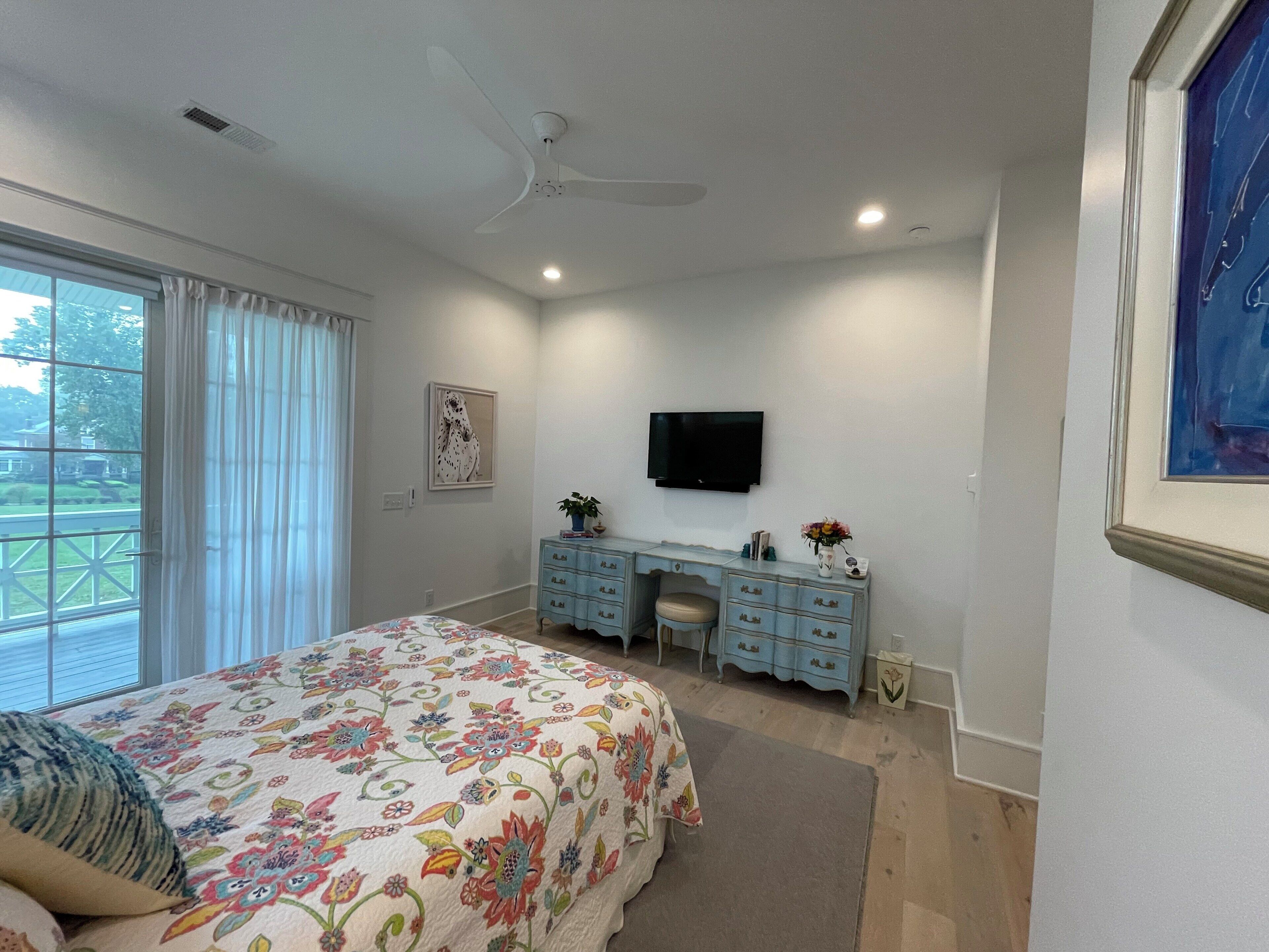 Un dormitorio con cama, cómoda, televisor y ventilador de techo.