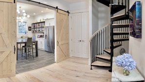 A modern kitchen with a sliding barn door entrance, a dining area with a table and chairs, and a black spiral staircase.