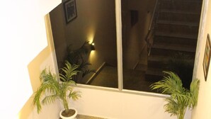 A staircase with metal railings, two potted plants, and a view of a staircase and a room with a bed and a lamp. - Red Crown Hotel (New Delhi)