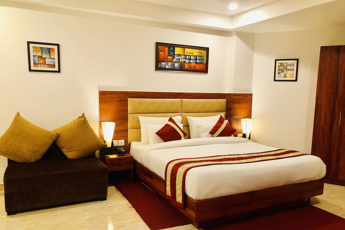 A hotel room with a large bed, a wooden headboard, a brown sofa, and two bedside lamps.