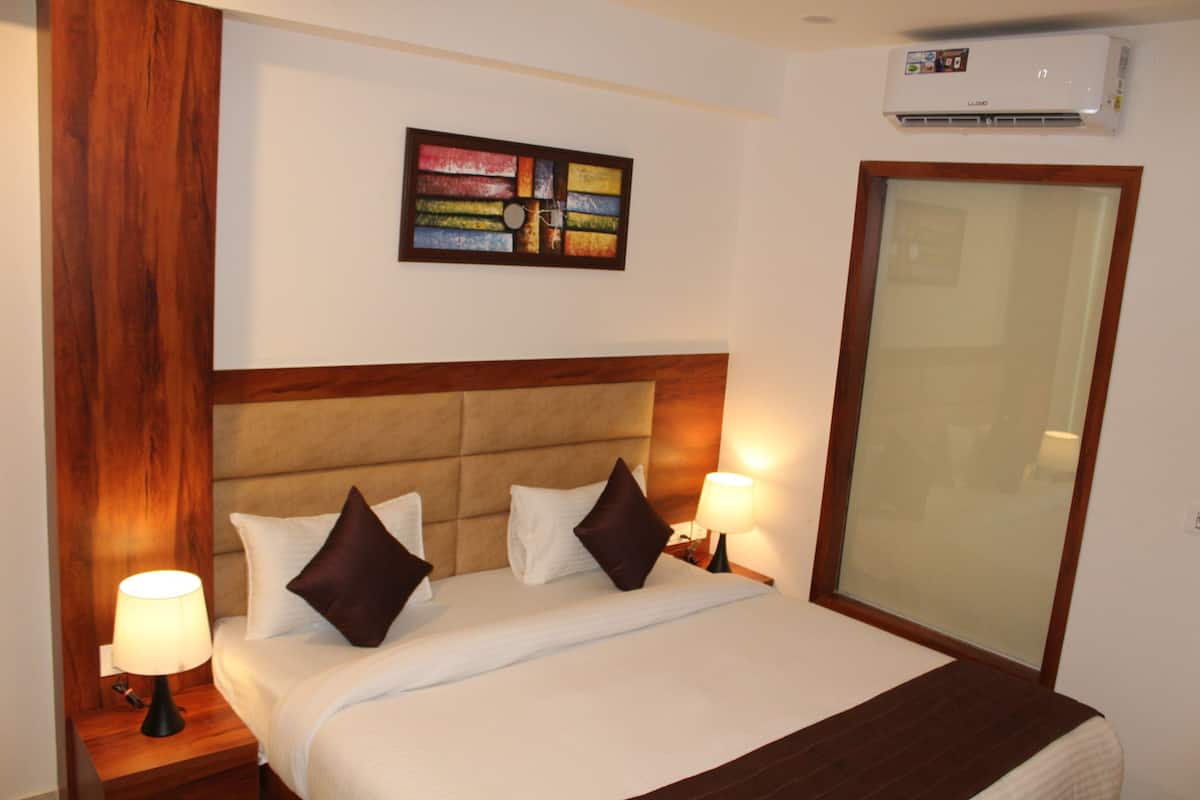A hotel room with a bed, two nightstands with lamps, a wall-mounted air conditioner, and a large mirror.