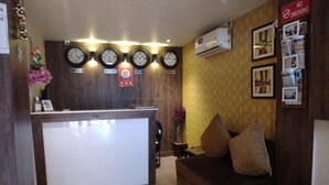 A reception area with a reception desk, clocks, a 'No Smoking' sign, and a couch with pillows. - Red Crown Hotel (New Delhi)