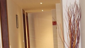A hallway with a wooden door on the left, a white vase with branches on the right, and a sign that says "EXTINGUISHER" on the wall. - Red Crown Hotel (New Delhi)