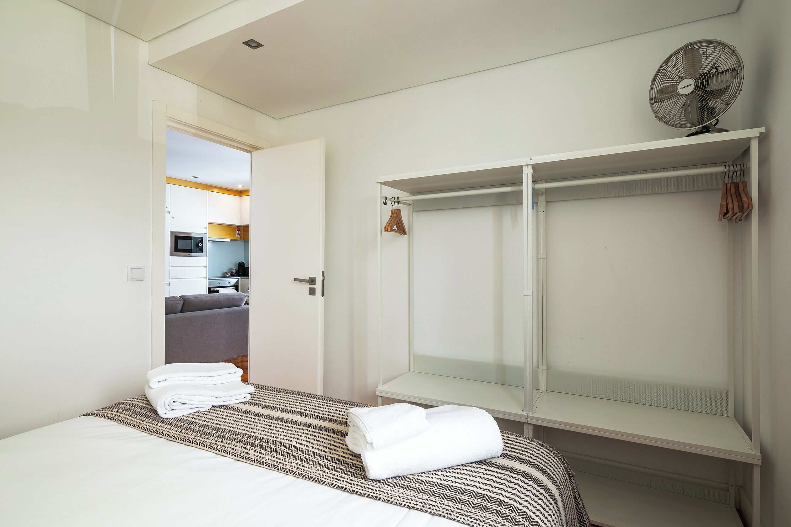 Une chambre d’hôtel moderne avec un lit bien fait, un dressing et, au fond, une petite cuisine.