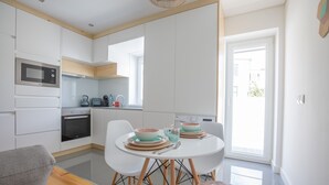 A modern kitchen with white cabinets, a built-in oven, and a dining area with a white table and chairs.