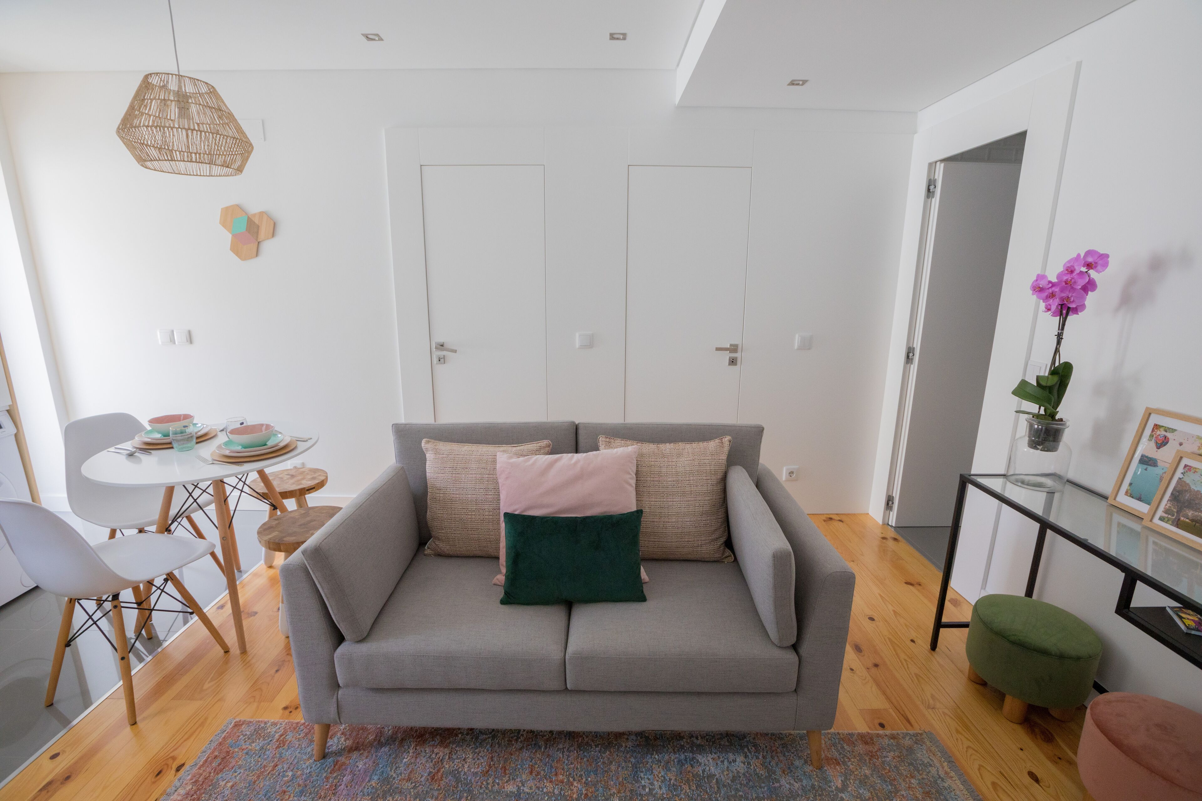 A modern living room with a grey sofa, a small round table, and a dining area with chairs.
