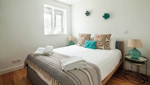 A bedroom with a large bed, a window, two wall-mounted flower decorations, and a bedside table with a lamp.