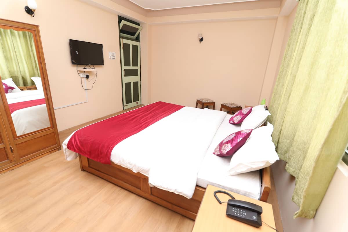 Un dormitorio con cama, televisor, mesita de noche, teléfono y ventana con cortinas.
