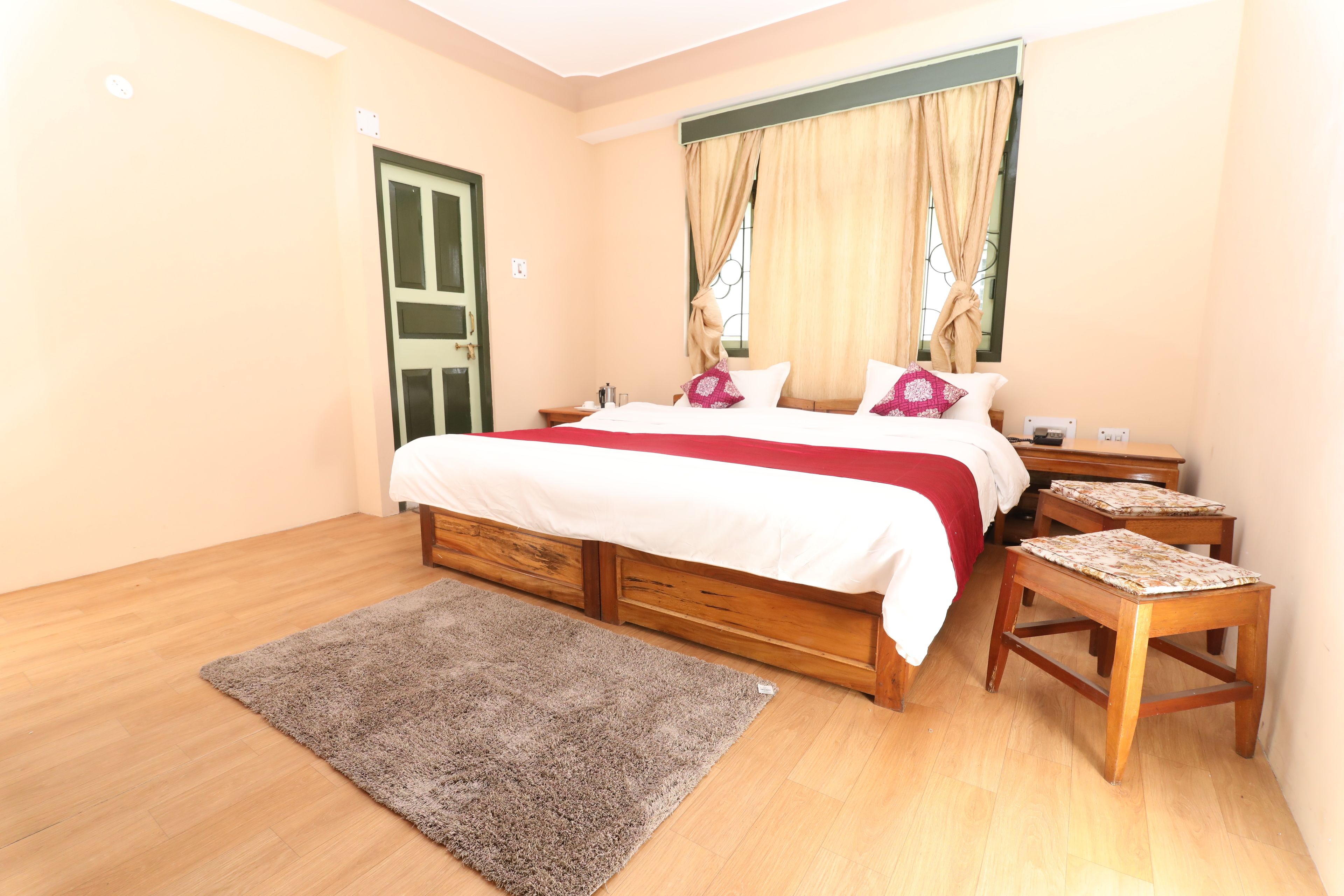 Un dormitorio con cama, mesitas de noche de madera, una pequeña mesa, un tapete y una ventana con cortinas.