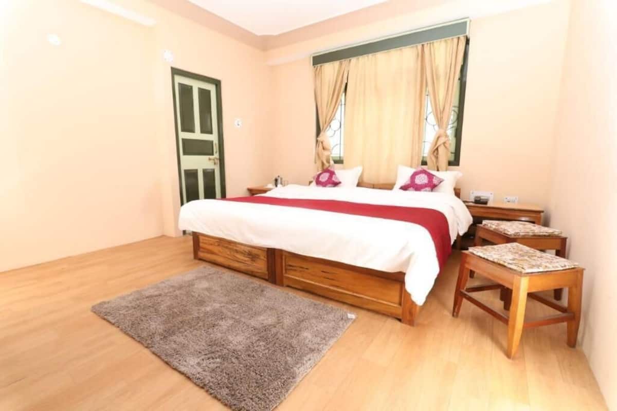 Un dormitorio con cama, mesitas de noche, alfombra y ventana con cortinas.