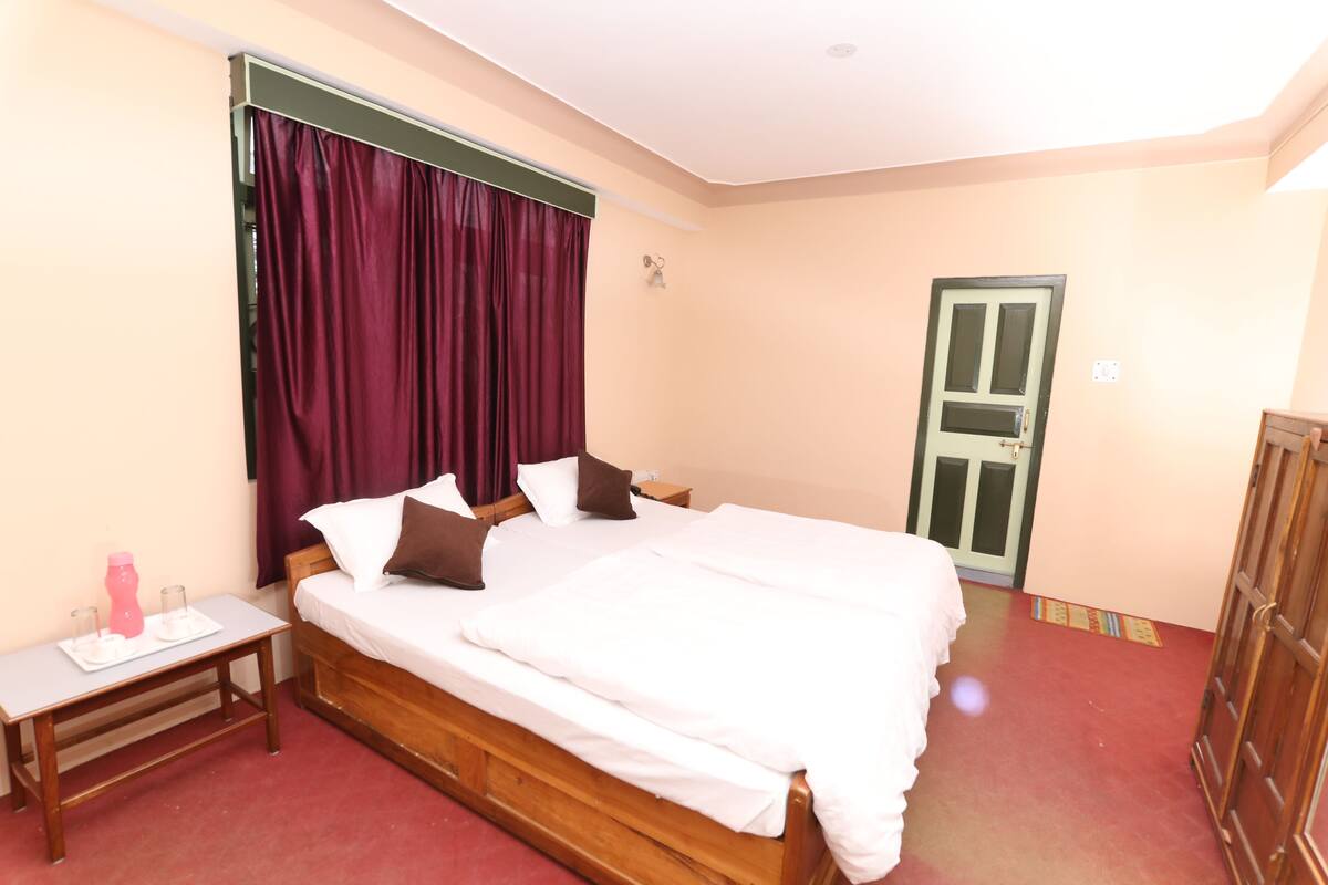 Un dormitorio con cama de madera, una mesita de noche, una ventana con cortinas y una puerta.