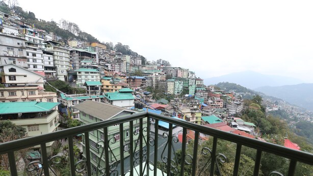 A hillside residential area with multi-story buildings, some with green roofs, and a balcony railing in the foreground. - Hotel Tenancy (Gangtok)