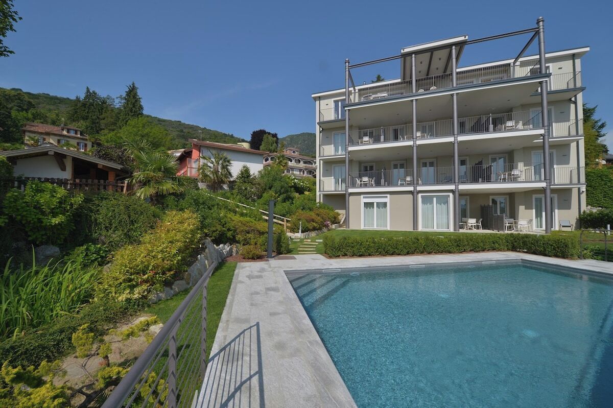 A multi-story hotel with a swimming pool, surrounded by greenery and hills.