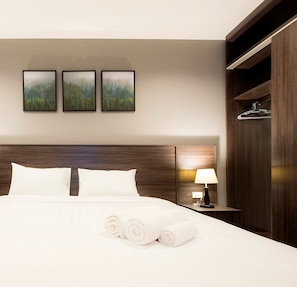 Une chambre d’hôtel avec un grand lit, deux oreillers, une table de chevet avec une lampe et trois tableaux encadrés accrochés au mur.