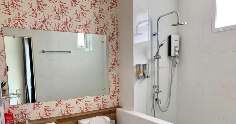 Un baño con un espejo grande, una ducha con cabezal de ducha manual y un inodoro.