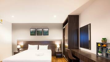 A modern hotel room with a large bed, two bedside tables with lamps, a desk with a chair, a wardrobe, and a shelf with decorative items.