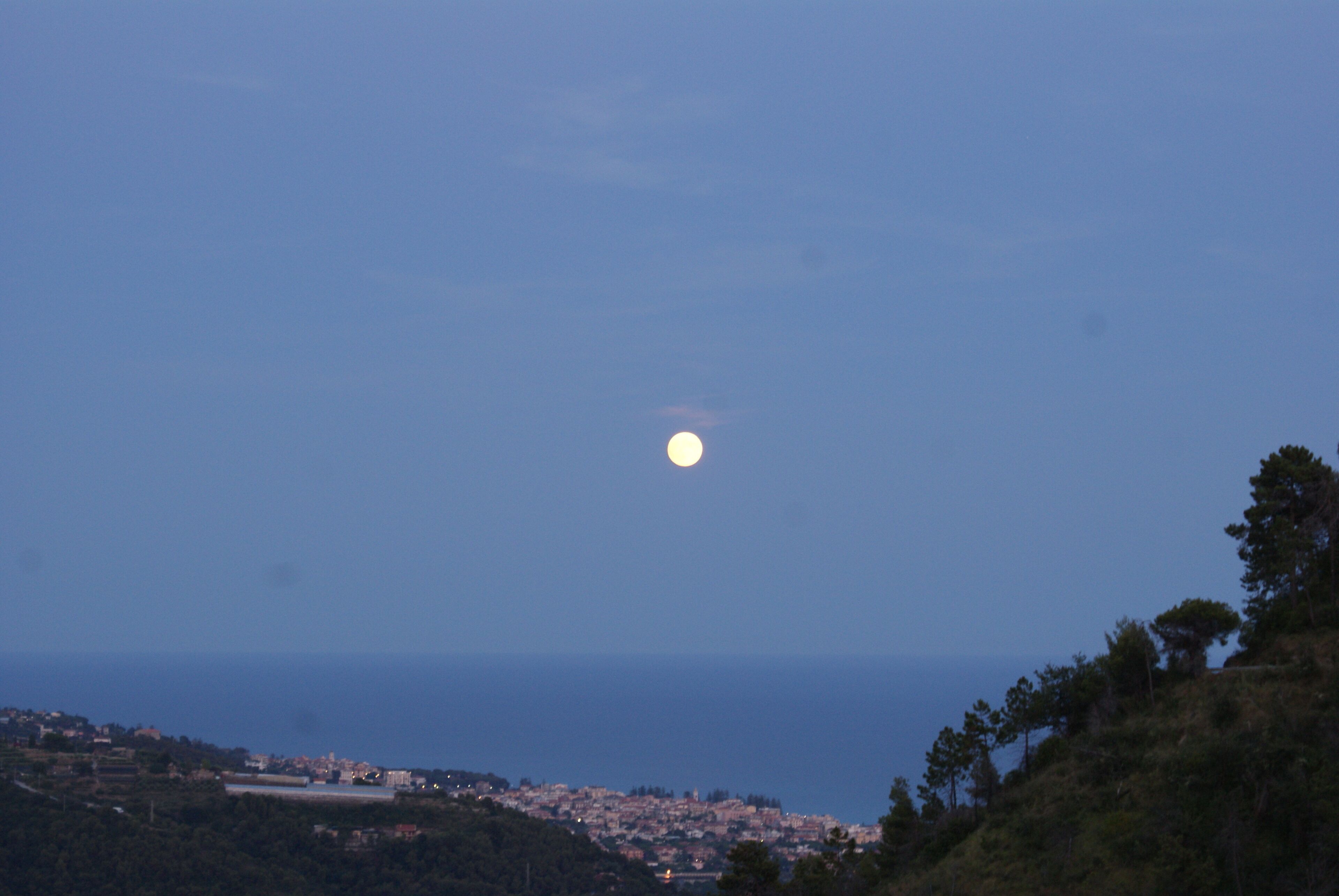A coastal town at dusk with a visible moon in the sky.