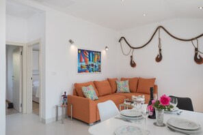 A modern living room with a sofa, a dining table set with plates and glasses, and a colorful painting on the wall. - Book Villa Basic and get relaxed with wine and beautiful sunset from top floor (Dvornica)