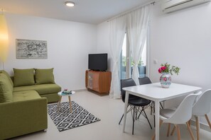 En moderne stue med en grøn sofa, et hvidt spisebord og et fjernsyn.