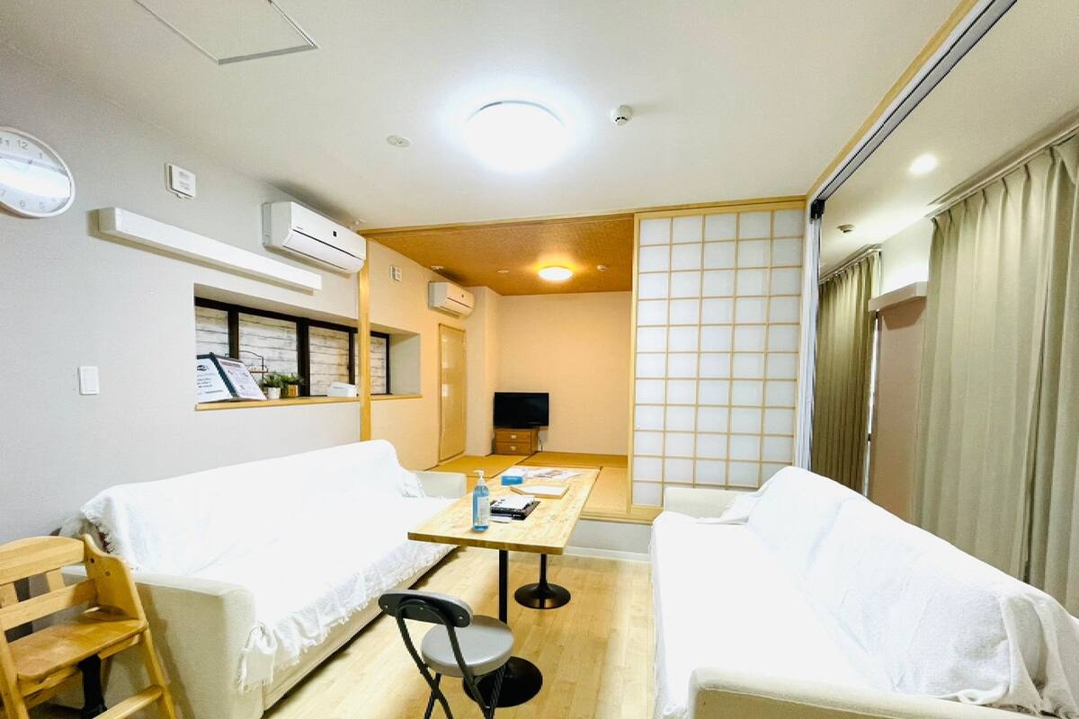 Quarto de hotel com duas camas, uma mesinha, uma cadeira, televisão e um painel deslizante shoji.