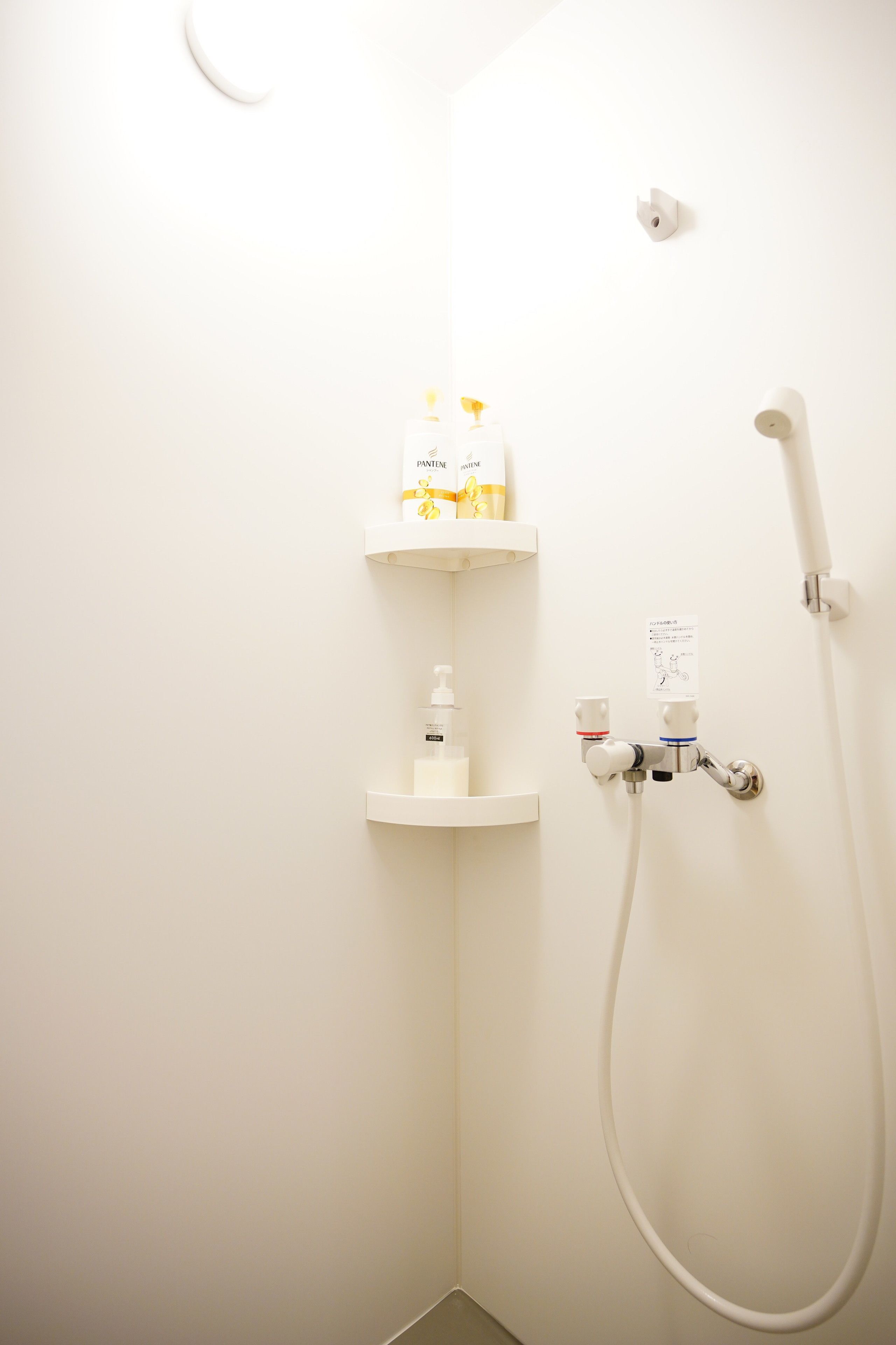 Un angolo doccia con soffione a mano, miscelatore a parete e due mensole bianche con articoli da toilette.