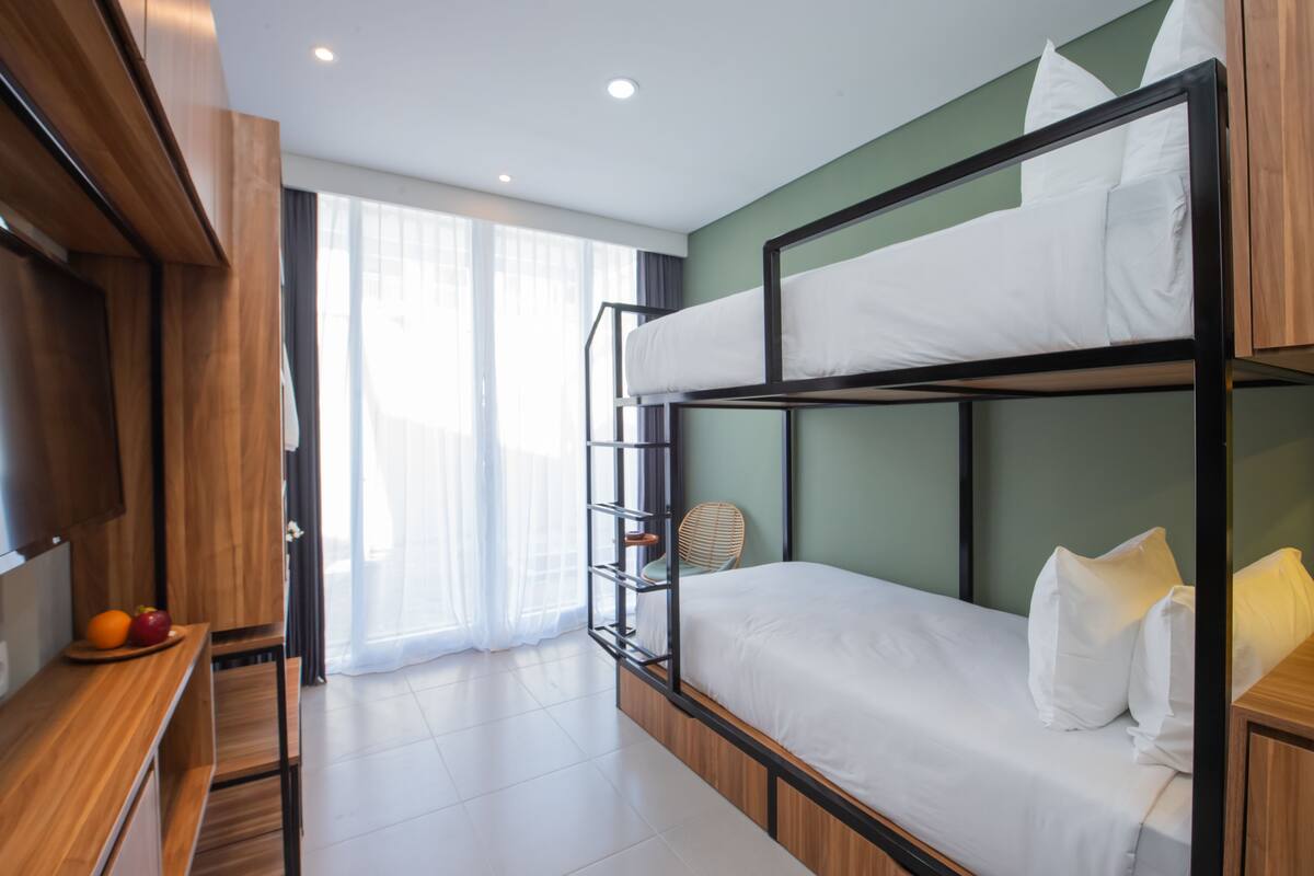 Quarto com beliche, uma escrivaninha de madeira, uma cadeira e uma mesinha com frutas.