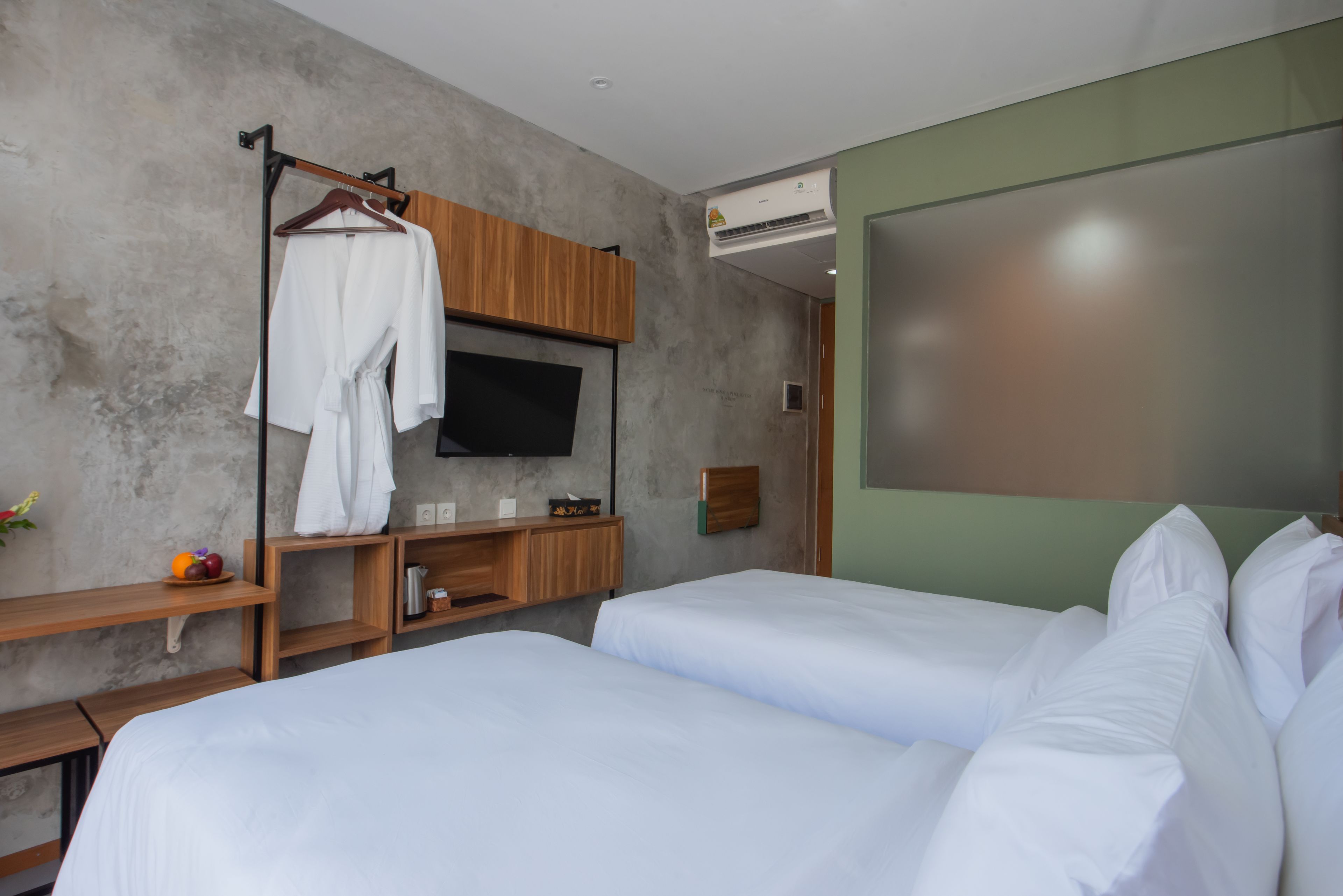Habitación de hotel con dos camas, un televisor, un estante de madera con bata y un aire acondicionado instalado en la pared.