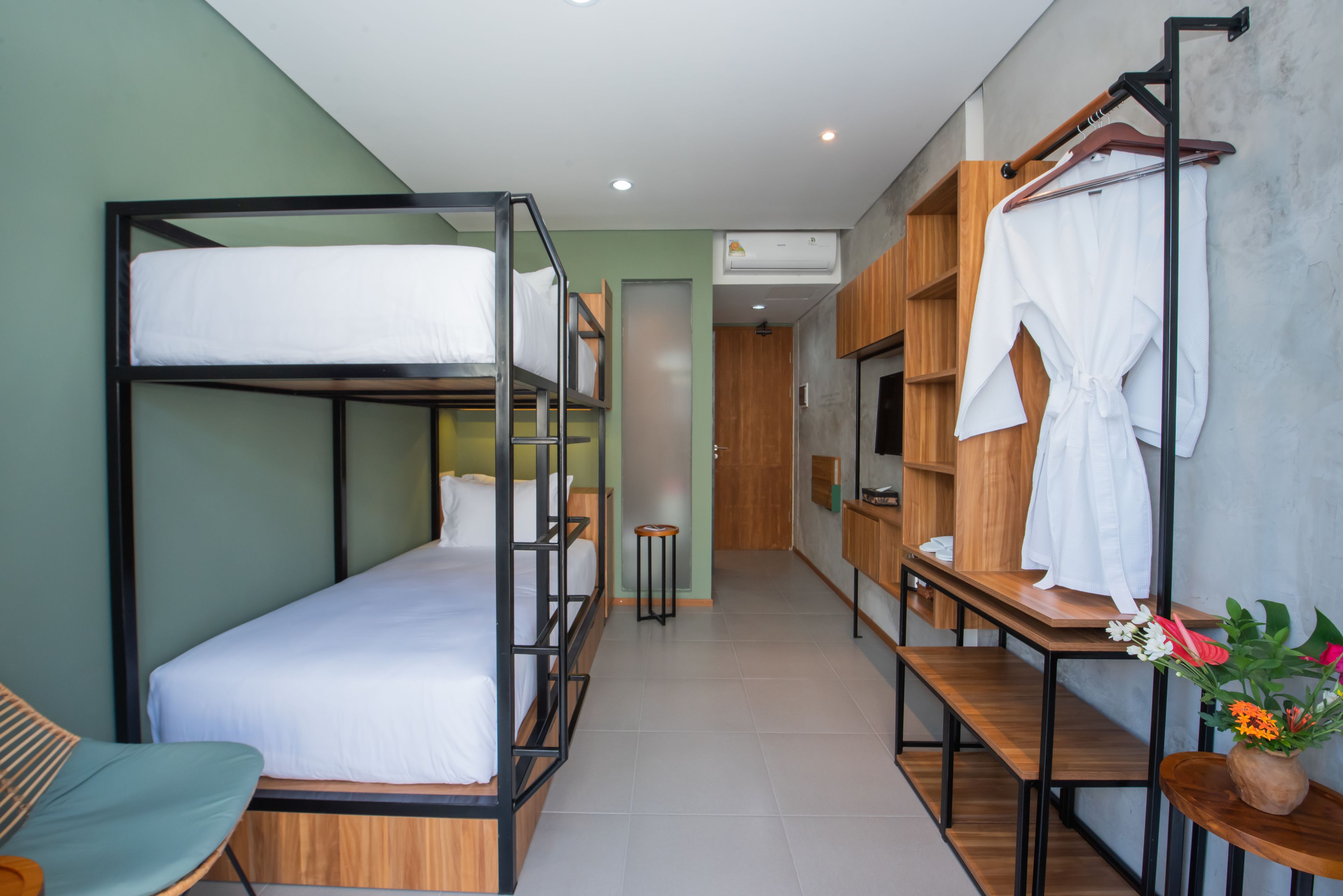 A bunk bed room with a wooden desk, a chair, and a hanging rack with clothes.