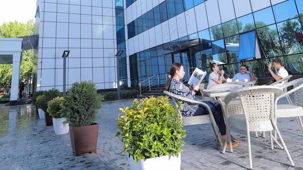 A modern building with reflective glass windows and a courtyard with outdoor seating. - Hilal Hotel Tashkent (Tashkent)