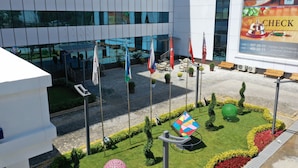 A modern building with multiple flags, a well-maintained garden, and a check-in sign. - Hilal Hotel Tashkent (Tashkent)