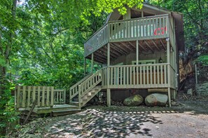 Une cabane en bois à plusieurs niveaux, dotée d’un escalier et d’une terrasse, entourée d’une forêt dense.