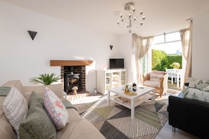 Relax in a stylish living room with a comfortable sofa, armchair, and fireplace, offering a view of lush greenery outside.