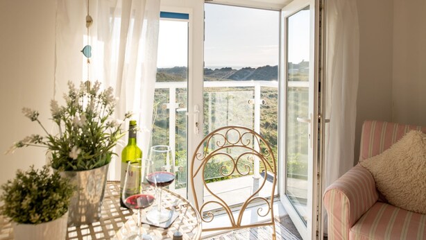A balcony with a table set for dining, a chair, and a sofa. - Lan y Môr : Family-Friendly 3‑Bed Cottage with Beach Access in Rhosneigr | Managed by Anglesey Holid (Rhosneigr)