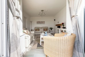 A living room with a sofa, a wicker chair, a coffee table, and a painting on the wall. - Lan Y Mor: The perfect escape amongst the dunes (Rhosneigr)