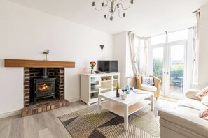 A living room with a fireplace, a television, a sofa, and a window with curtains. - Lan Y Mor: The perfect escape amongst the dunes (Rhosneigr)
